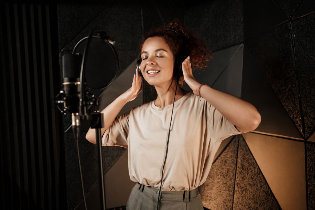 linda-cantora-sorridente-em-fones-de-ouvido-gravando-sonhadoramente-nova-musica-em-estudio-profissional-resized